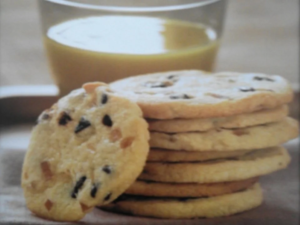 Mr Bake chocolate chip biscuits stacked beside a glass of milk.
